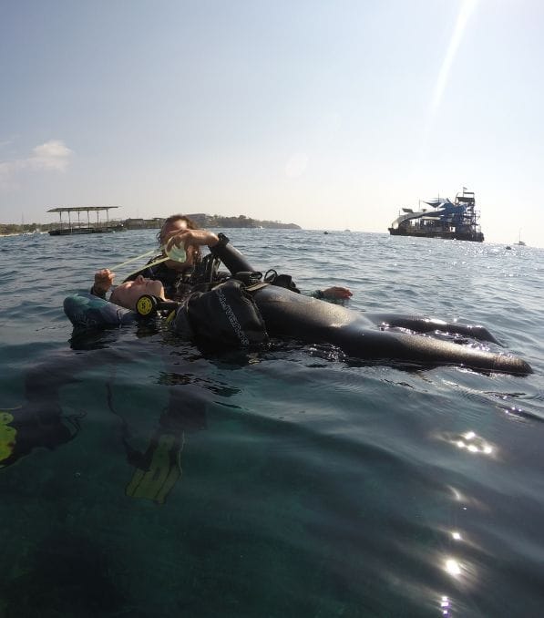 Rescue – 2 潜水员在努沙佩尼达(Nusa Penida)海面上做漂浮求生训练,一人仰躺接受另一人供气面罩支持,远处有船只。